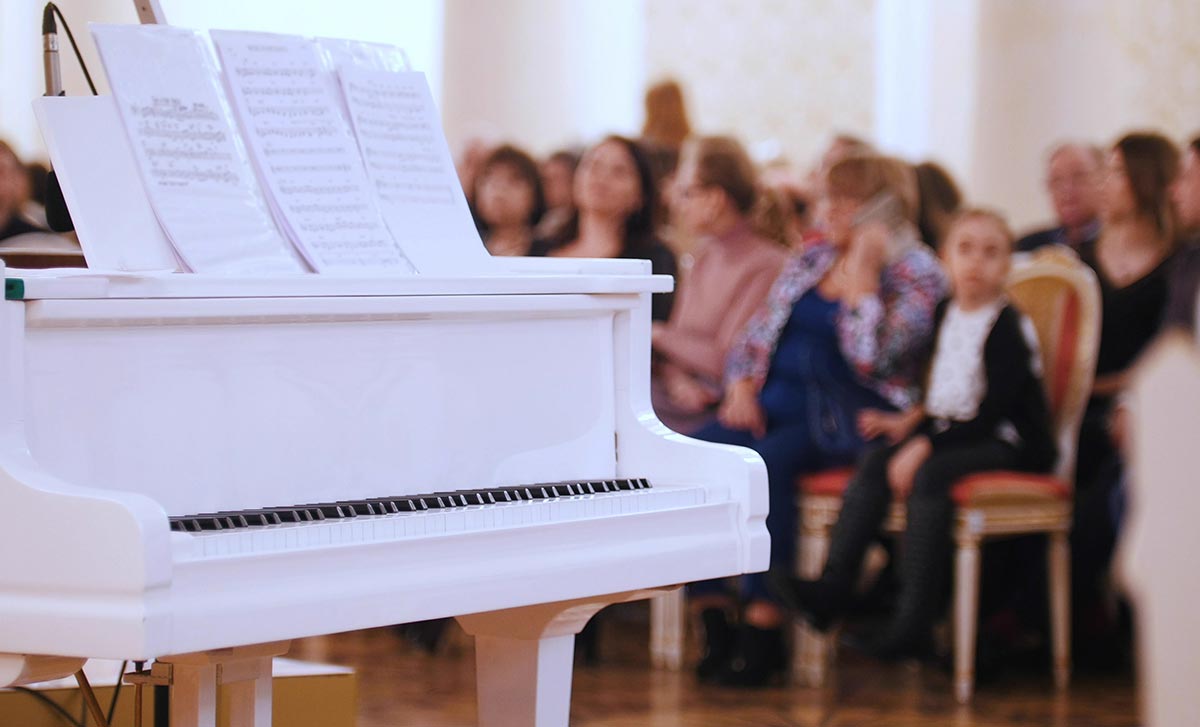 White color grand piano on stage with audience on the background