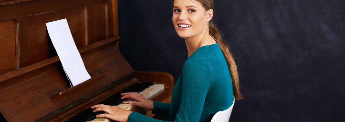 Adult piano student smiling while practising at an upright piano during a music lesson