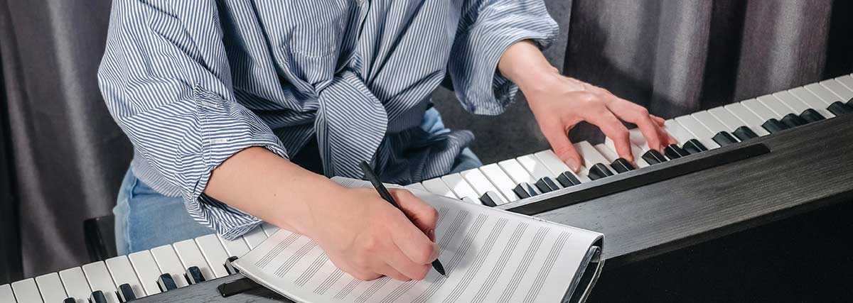 Pianist writing practice notes while playing a digital piano to build consistent piano practice habits