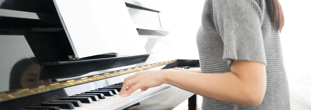 Adult woman playing an upright piano in a bright room