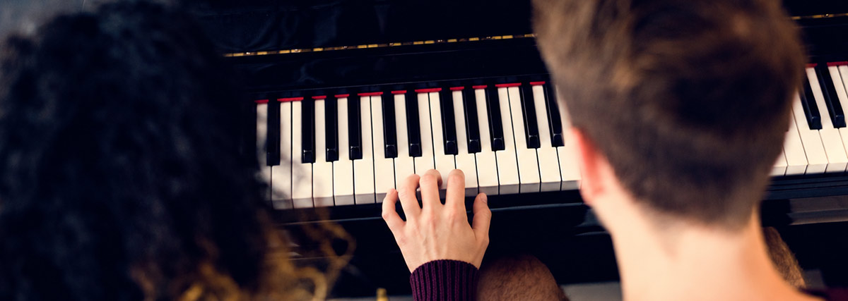 Two people exploring piano technique at an upright piano